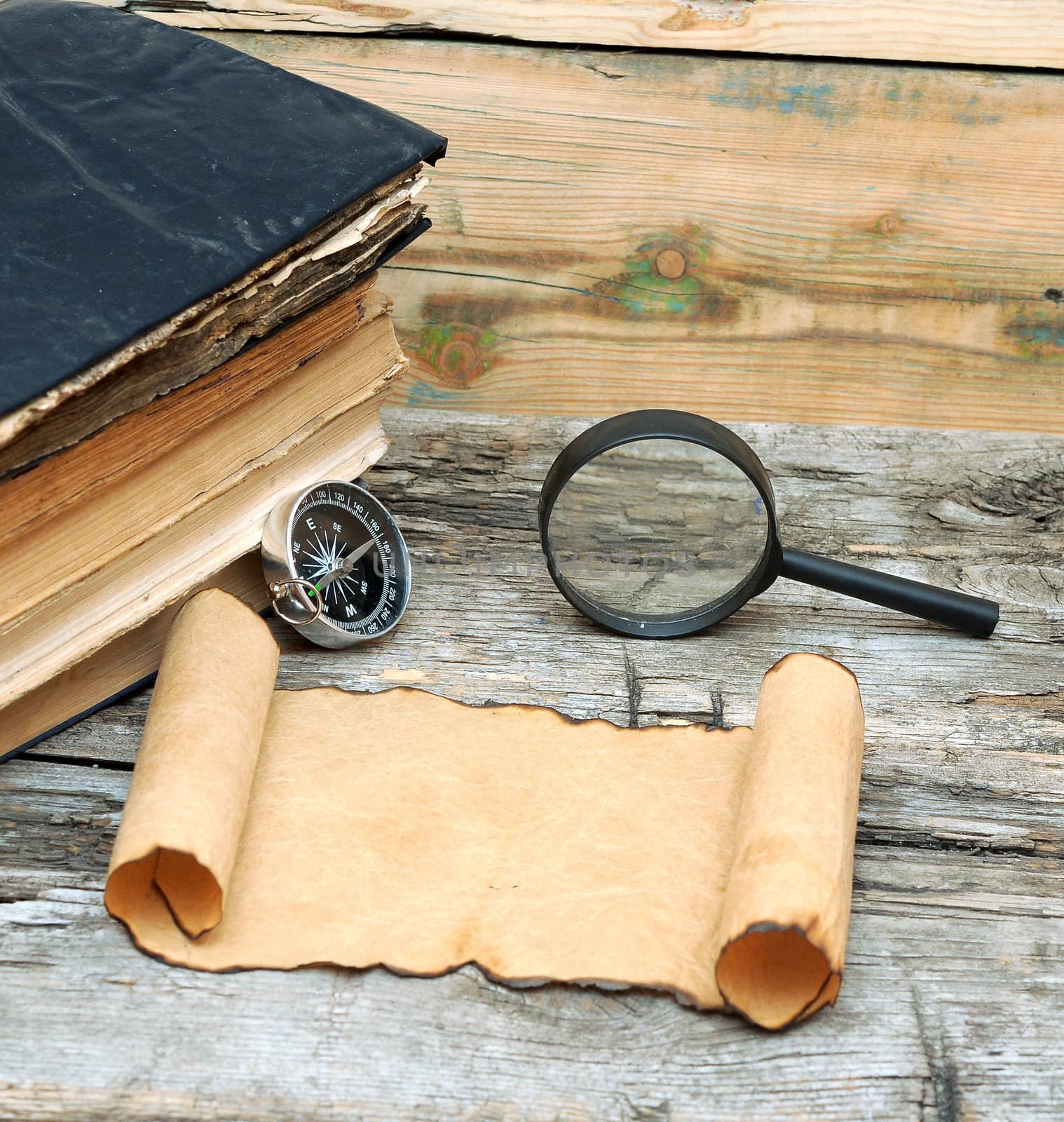 Stack of antique books with compass, magnifying glass and paper scroll on wood background