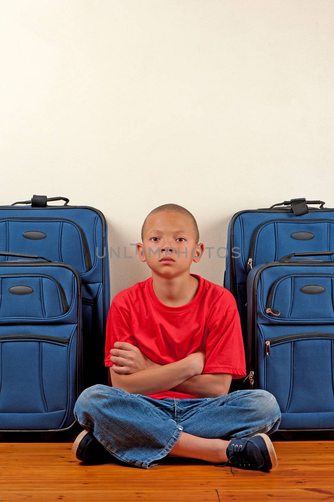 A boy sitting in front of suitcases appears upset.