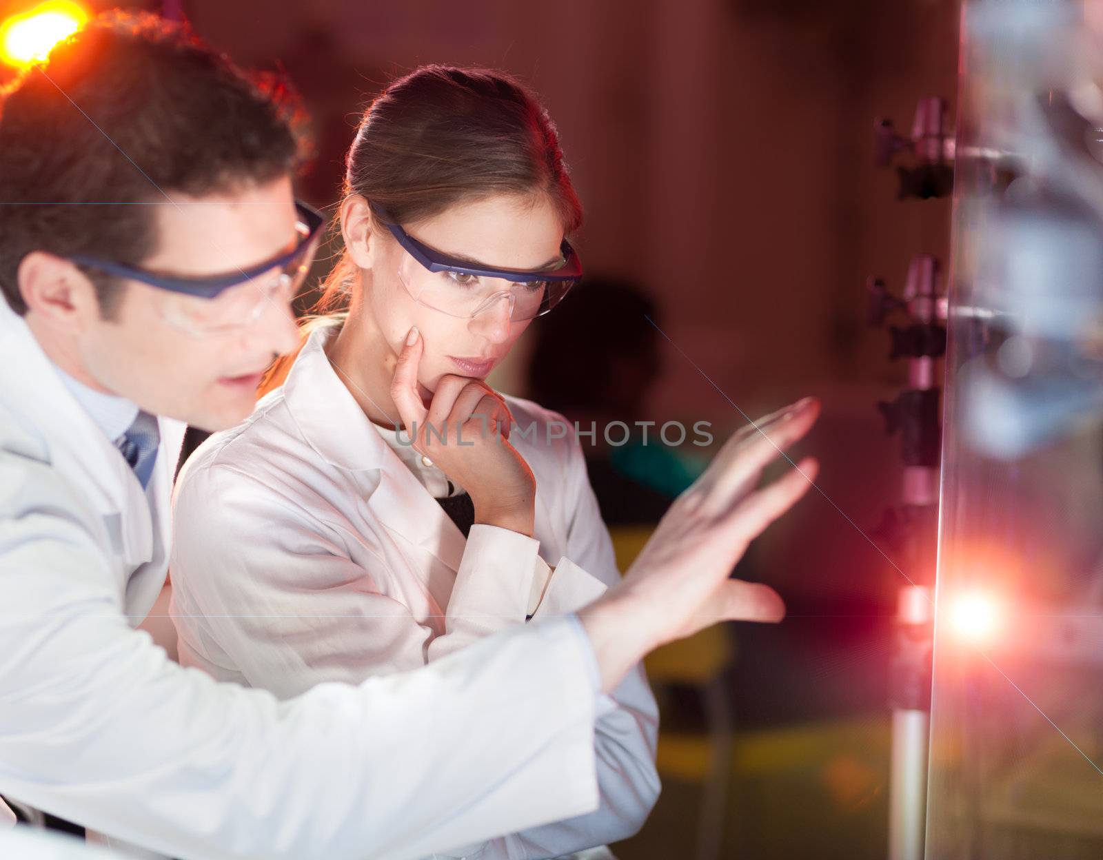 Portrait of a focused electrical engineering researchers in their working environment checking the phenomenon of breaking laser beam on the glass surface.