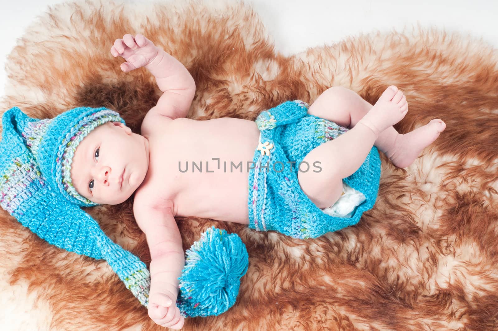 Newborn baby in long knitted hat on fur