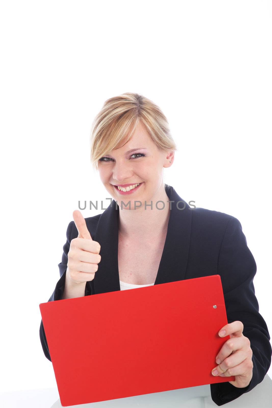 Happy young businesswoman with a beaming smile giving a thumbs up of success after reading notes on the red clipboard she is holding