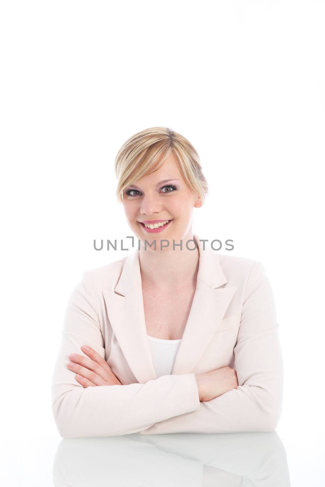 Light bright portrait of a charming businesswoman in a white jacket sitting at a desk with her arms folded smiling at the camera