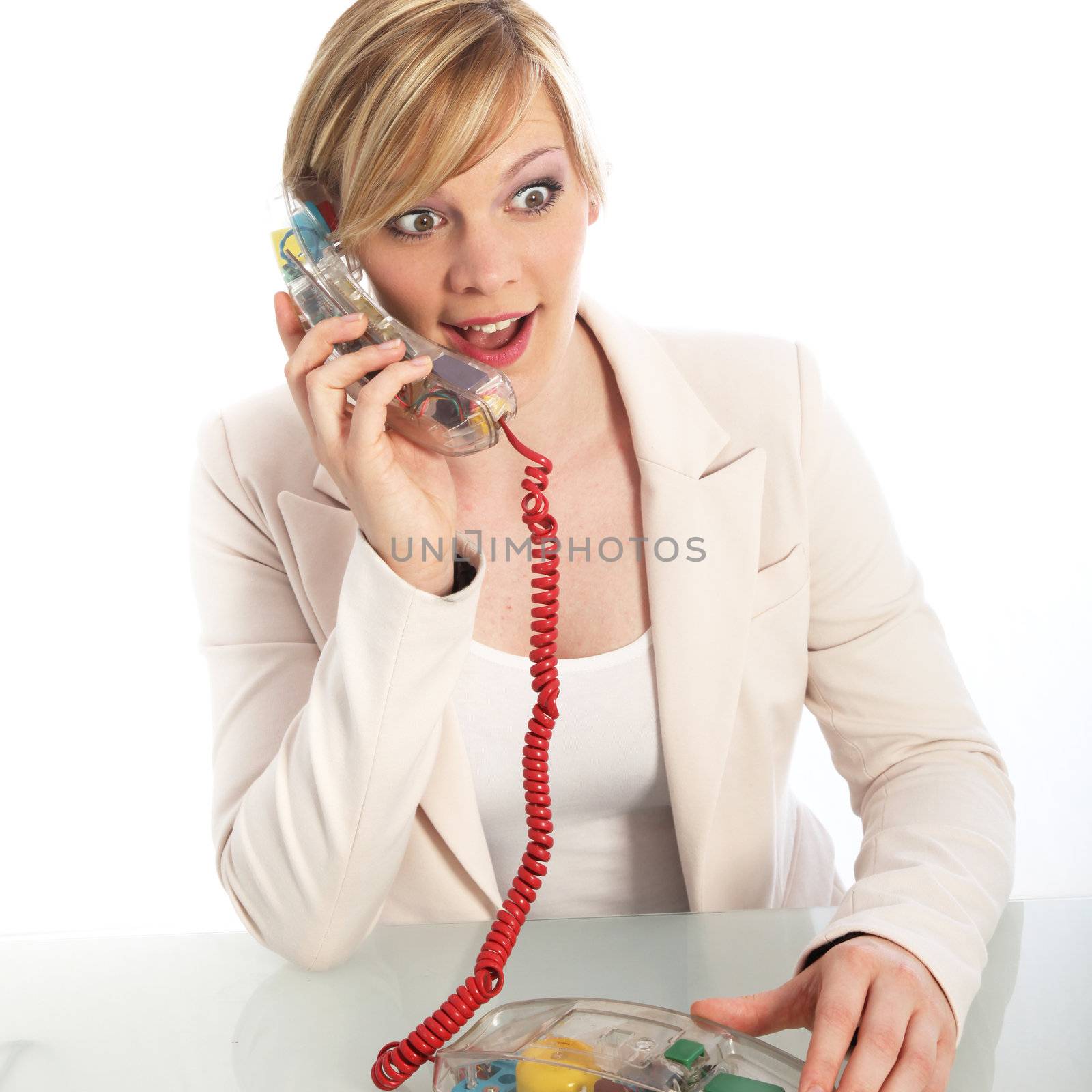 Surprised young woman with a wide-eyed expression talking on a landline telephone while sitting at a table