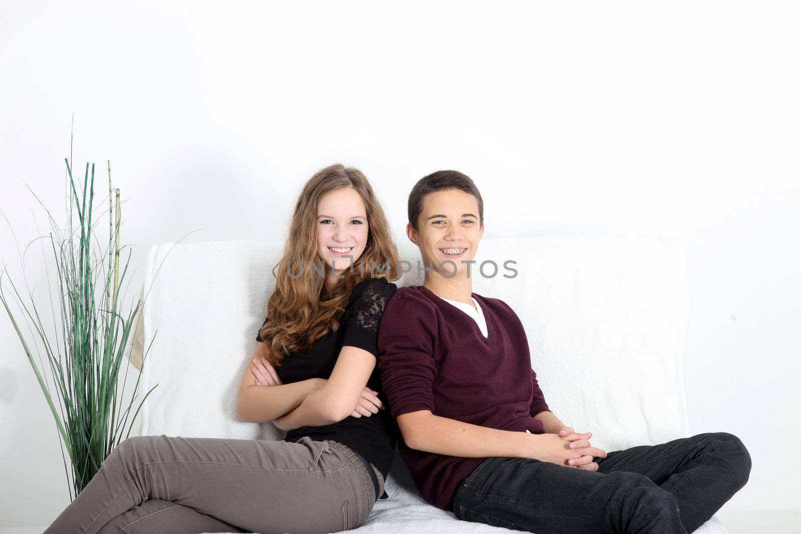 Young attractive smiling teenaged couple in trendy clothes relaxing at home reclining on a white sofa with copyspace