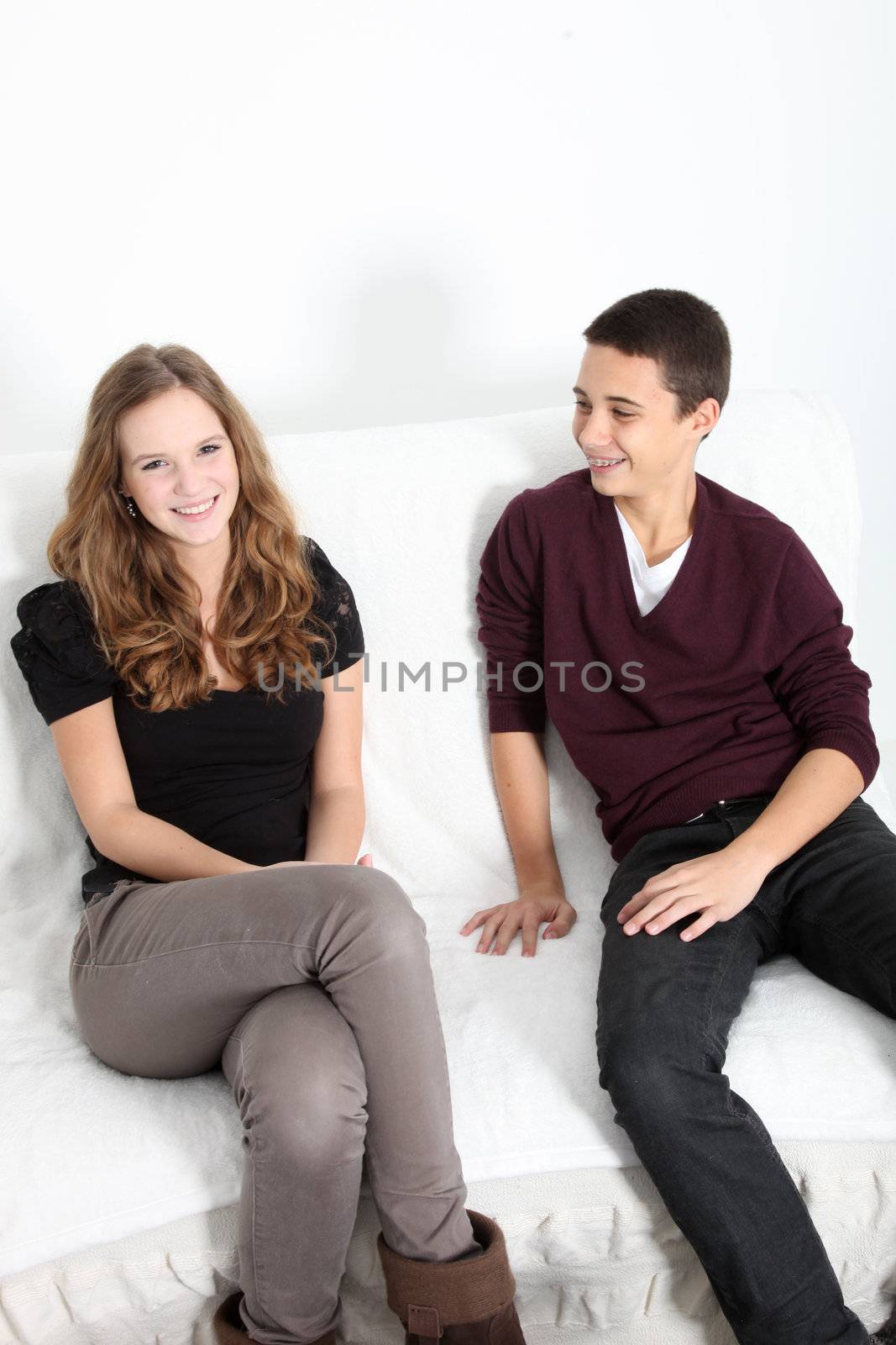 Attractive trendy young teenage brother and sister relaxing at home sitting enjoying themselves on a couch