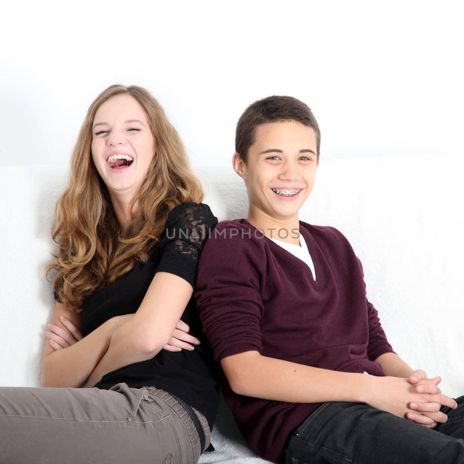 Laughing teenaged brother and sister sitting leaning on each other enjoying a good joke, square format with copyspace