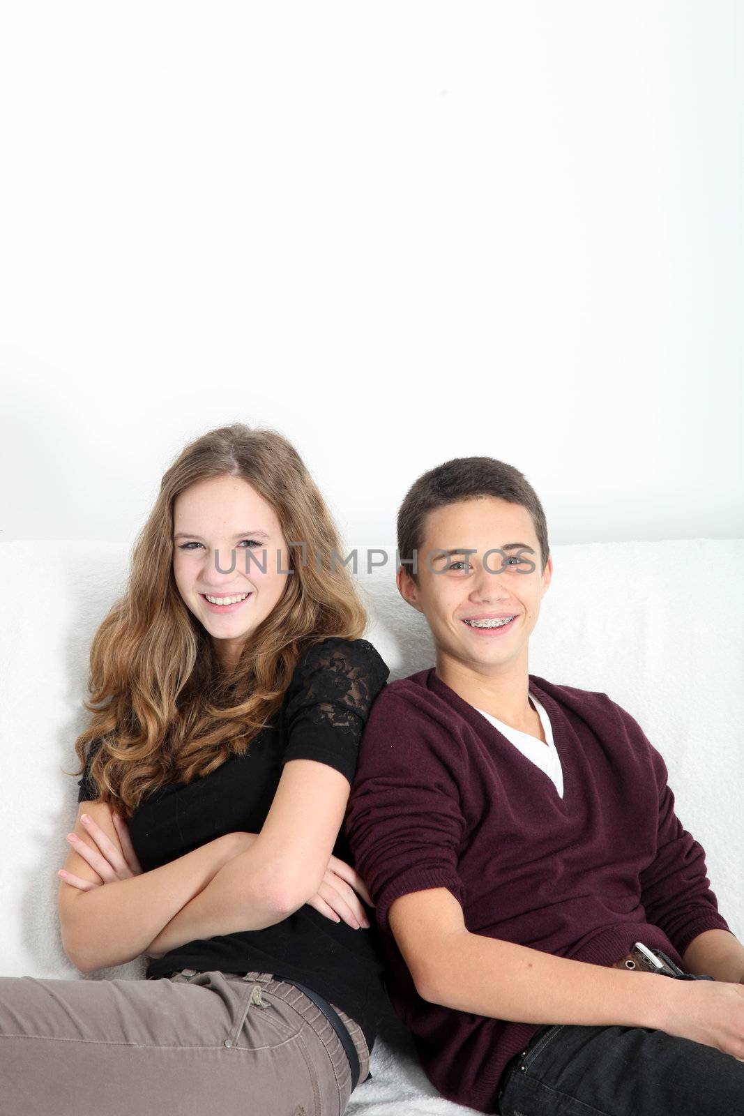 Happy attractive teenage couple sitting together on a couch with overhead copyspace smiling charmingly at the camera