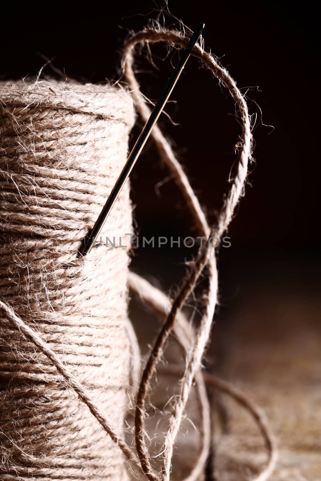 Artistic image of spool of thread and needle over wooden surface