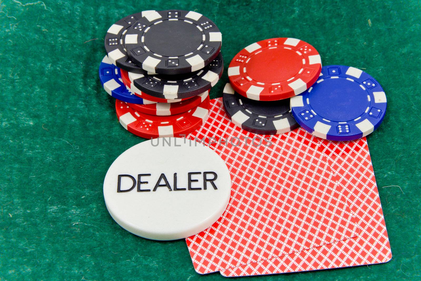 cards and stack of Poker chips and dealer button on a green background
