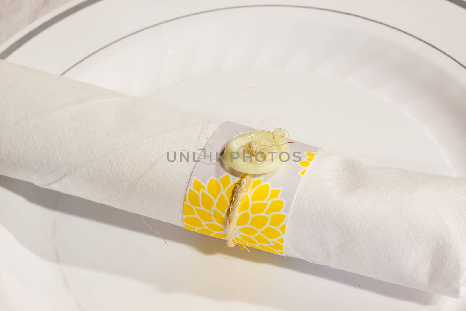 Silverware is wrapped up in a napkin for a wedding dinner reception in an old barn. The wedding decor includes a japanese or chinese influence with colors of white, grey (or gray) and yellow. They used twine to wrap up the place settings.