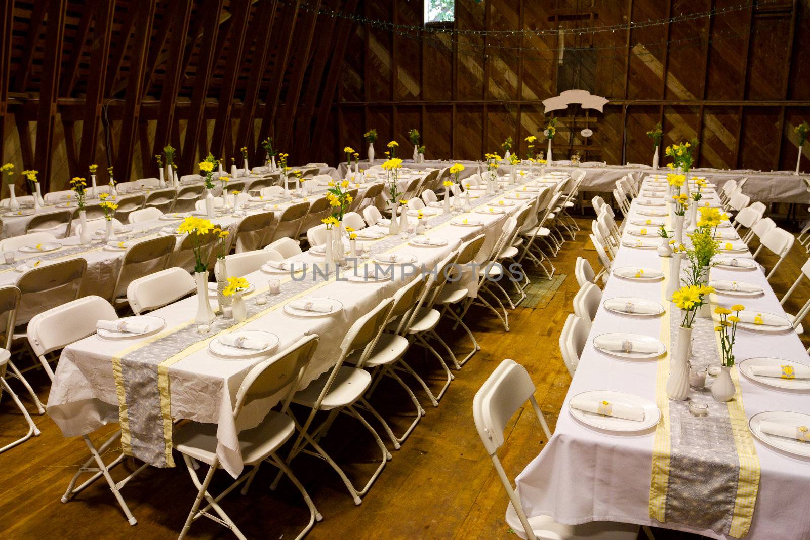 Tables are set up in an old barn for a wedding reception including dinner. These rows of tables are ready to seta and serve plenty of guests at this elegant diy wedding in the country.