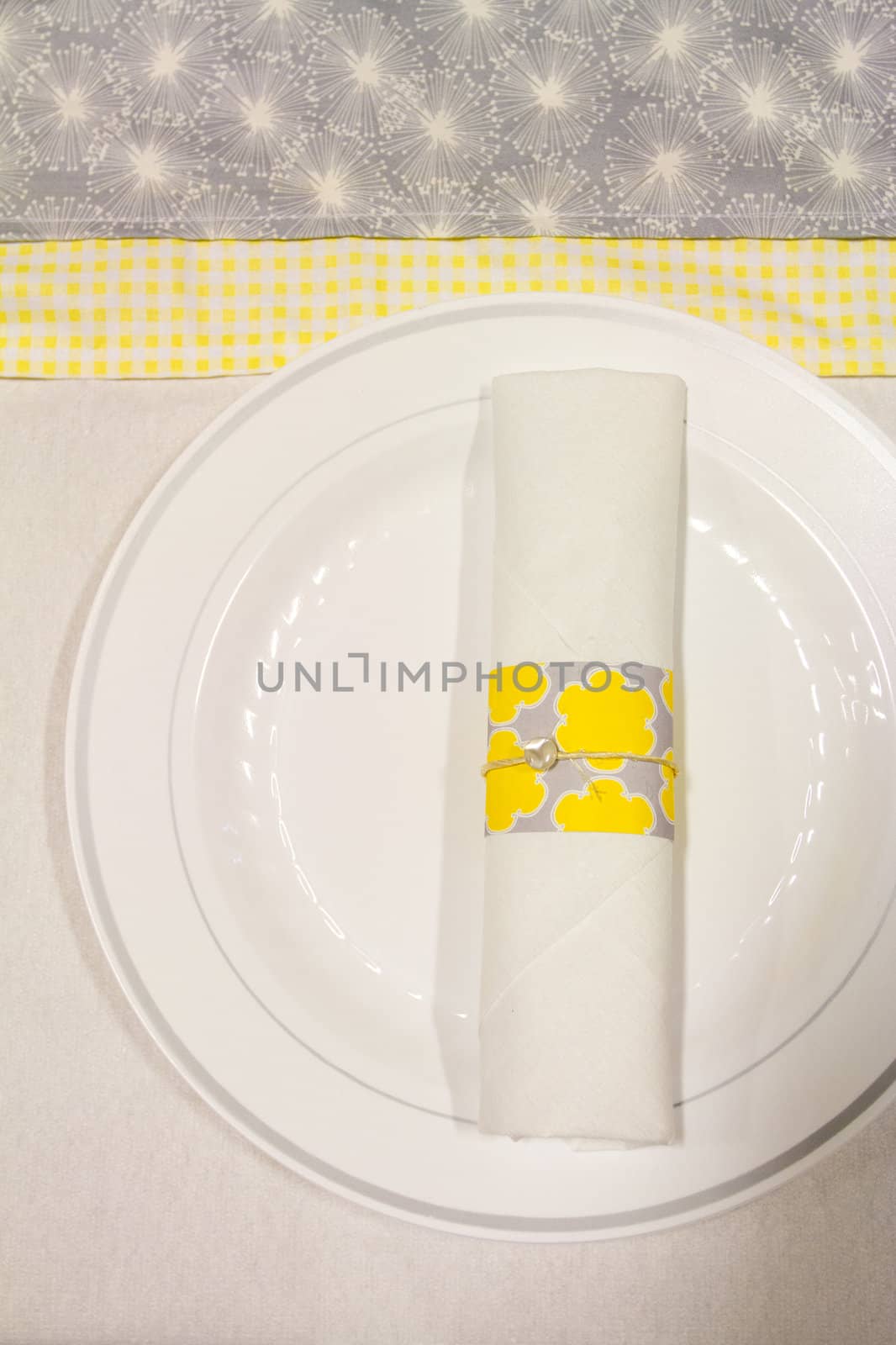 Silverware is wrapped up in a napkin for a wedding dinner reception in an old barn. The wedding decor includes a japanese or chinese influence with colors of white, grey (or gray) and yellow. They used twine to wrap up the place settings.