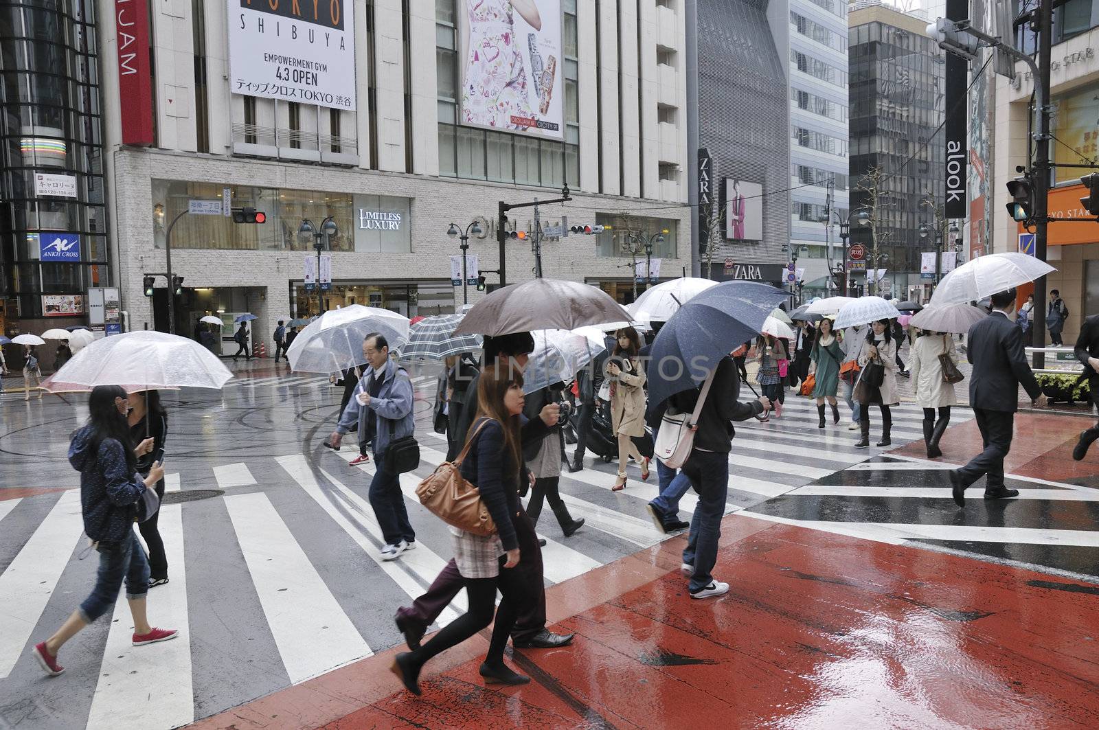 TOKYO, JAPAN -APRIL 23, 2011 : people cross over street in Tokyo Shibuya area under rain. Shibuya district is very famous for it's fashion shops and crowds of young people.