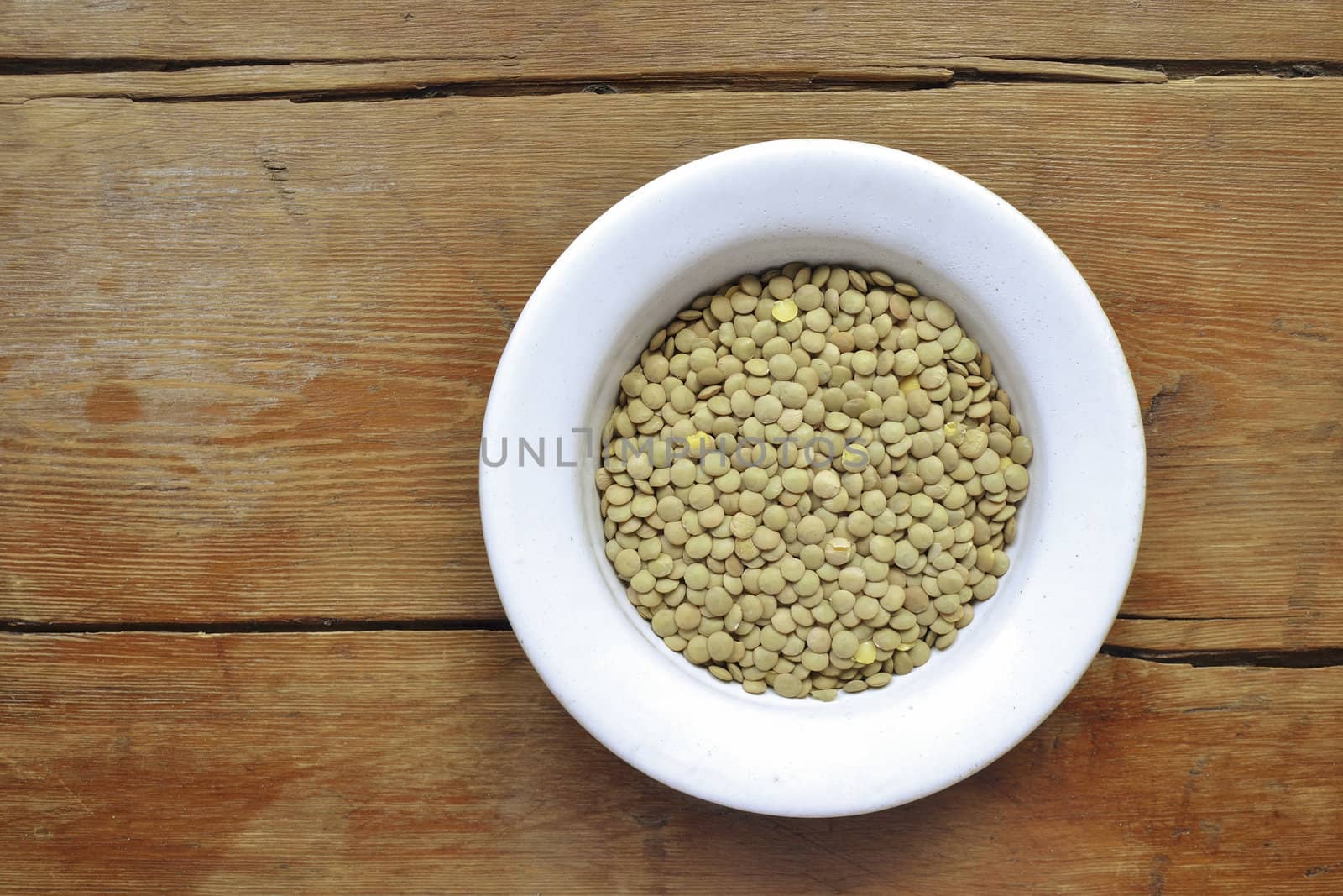 raw dry lentil beans in white bowl on vintage wooden table; focus on lentil