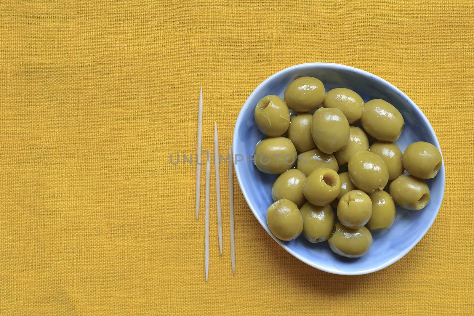 pitted green olives on blue plate over yellow tablecloth