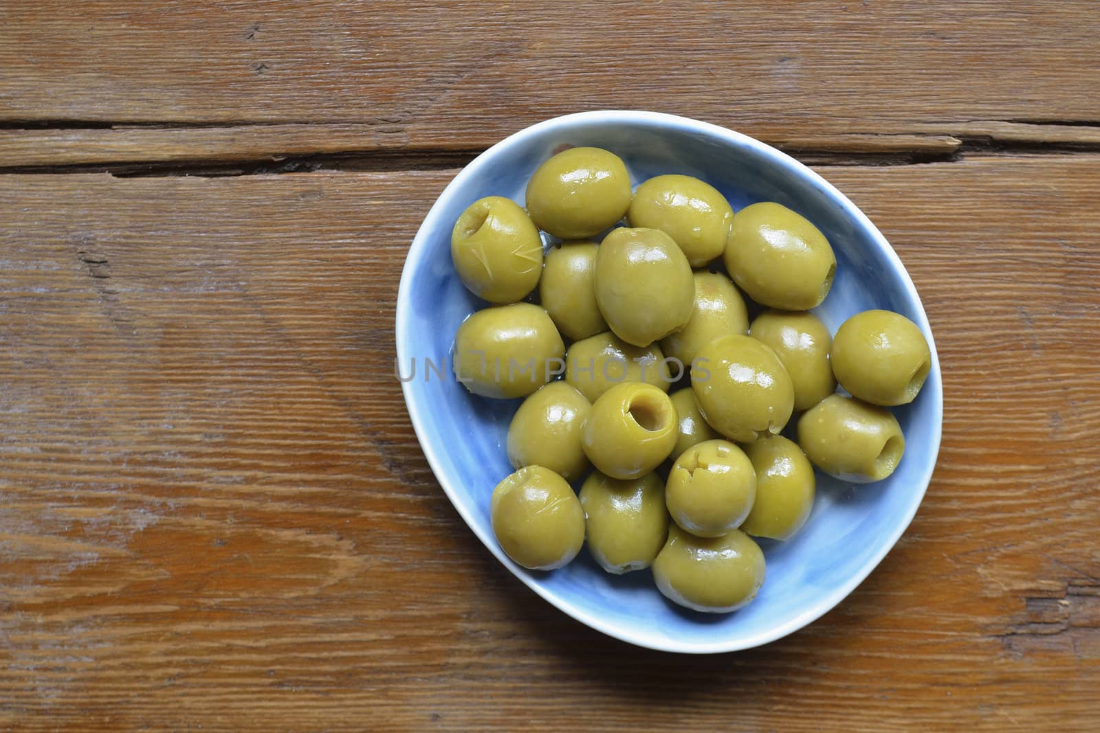 pitted green olives on blue plate over weathered wooden table; focus on olives