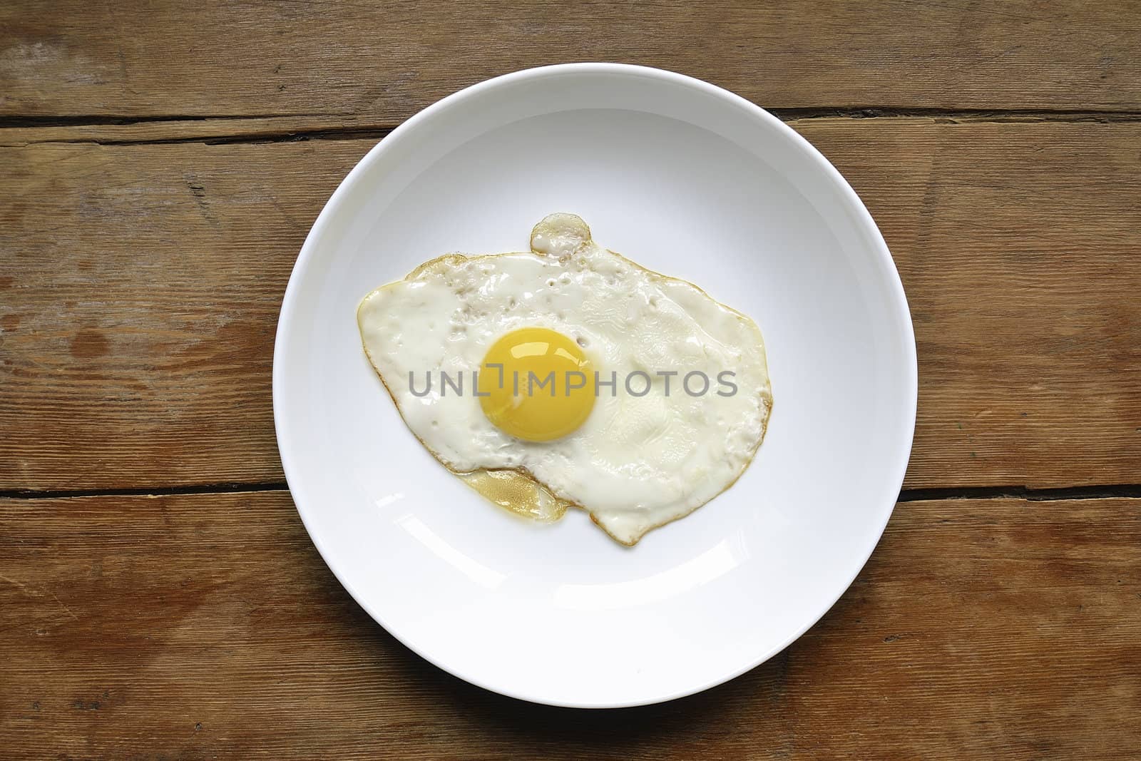 white plate with fresh fried egg on the vintage wooden table