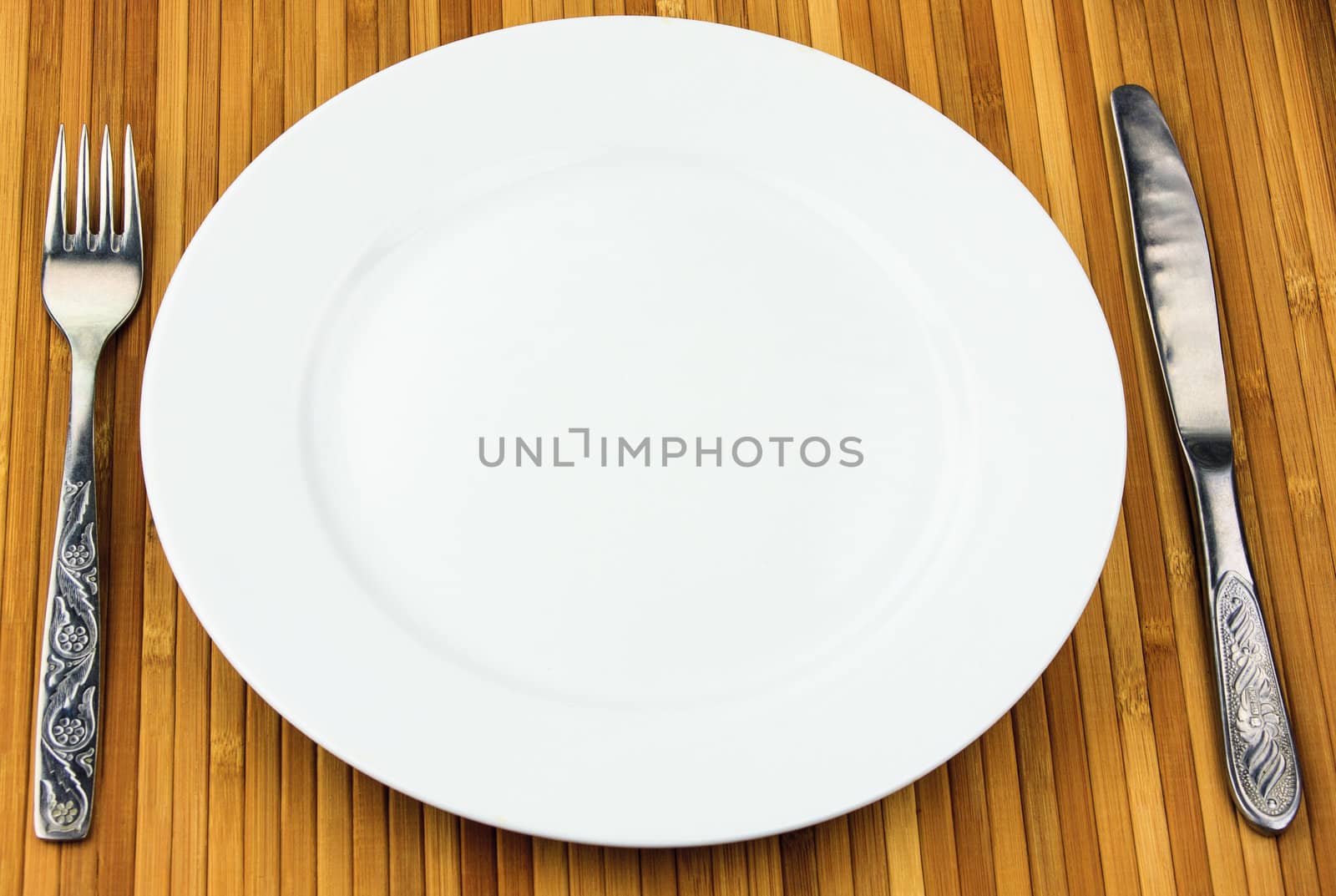 white plate, knife and fork at bamboo napkin by sfinks