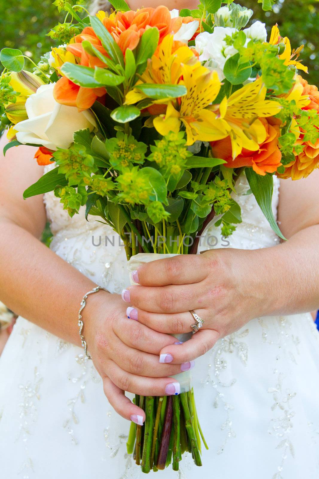 A bride in her white wedding dress holds her bouquet of orange, green, and yellow flowers on her wedding day.