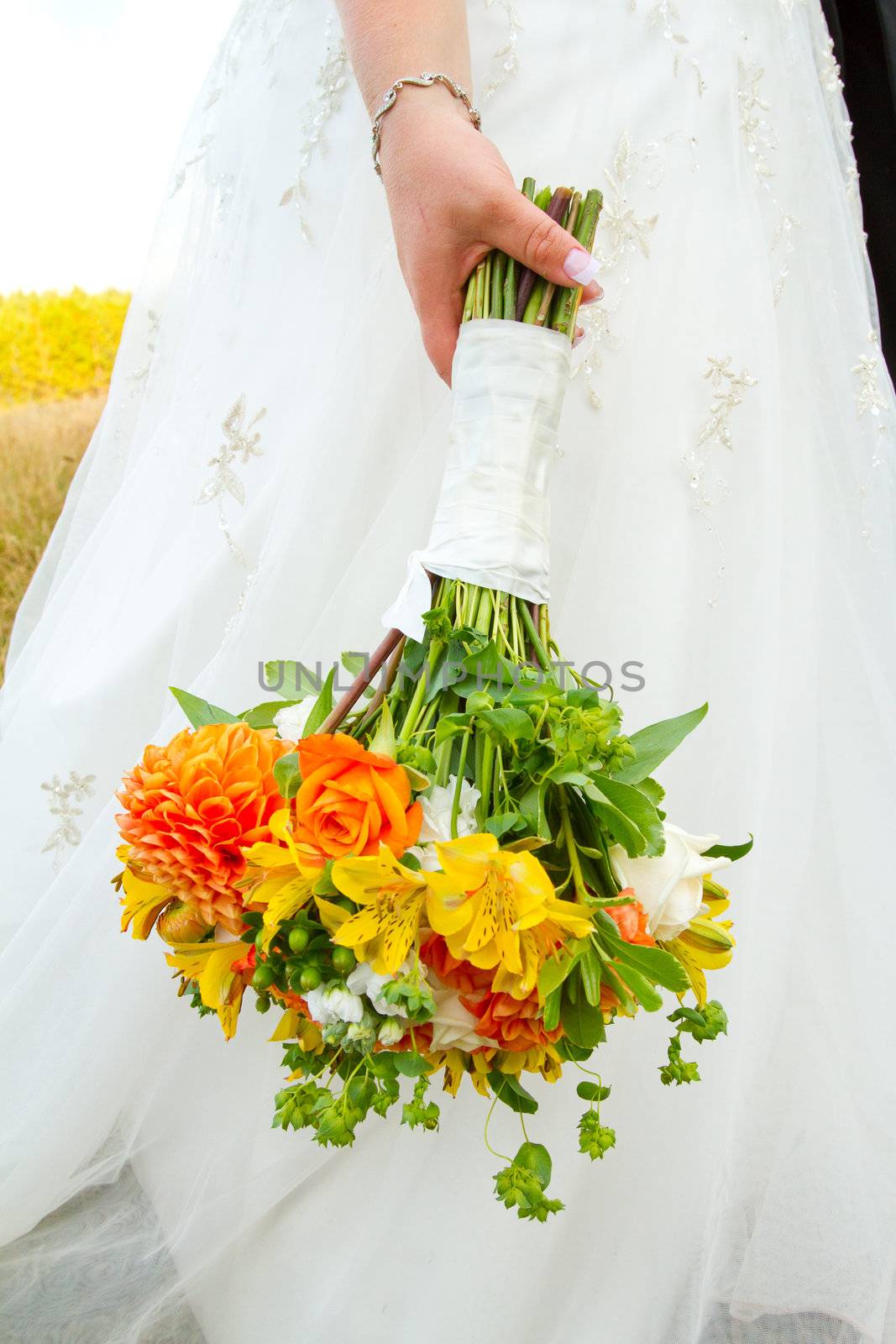 A bride in her white wedding dress holds her bouquet of orange, green, and yellow flowers on her wedding day.