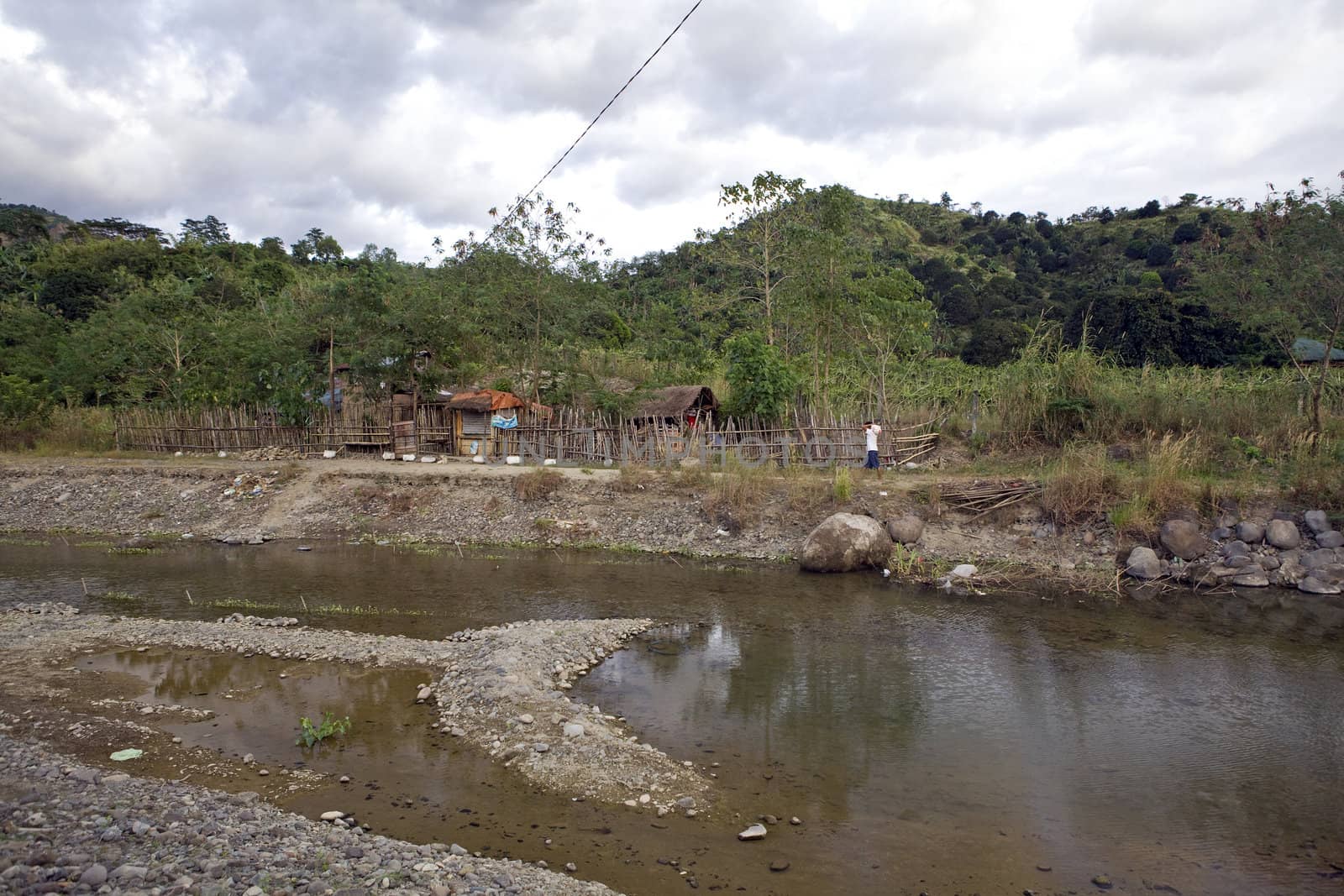 A Philippine Island village home made of sticks, bamboo and coconut tree leaves sits beside a river.