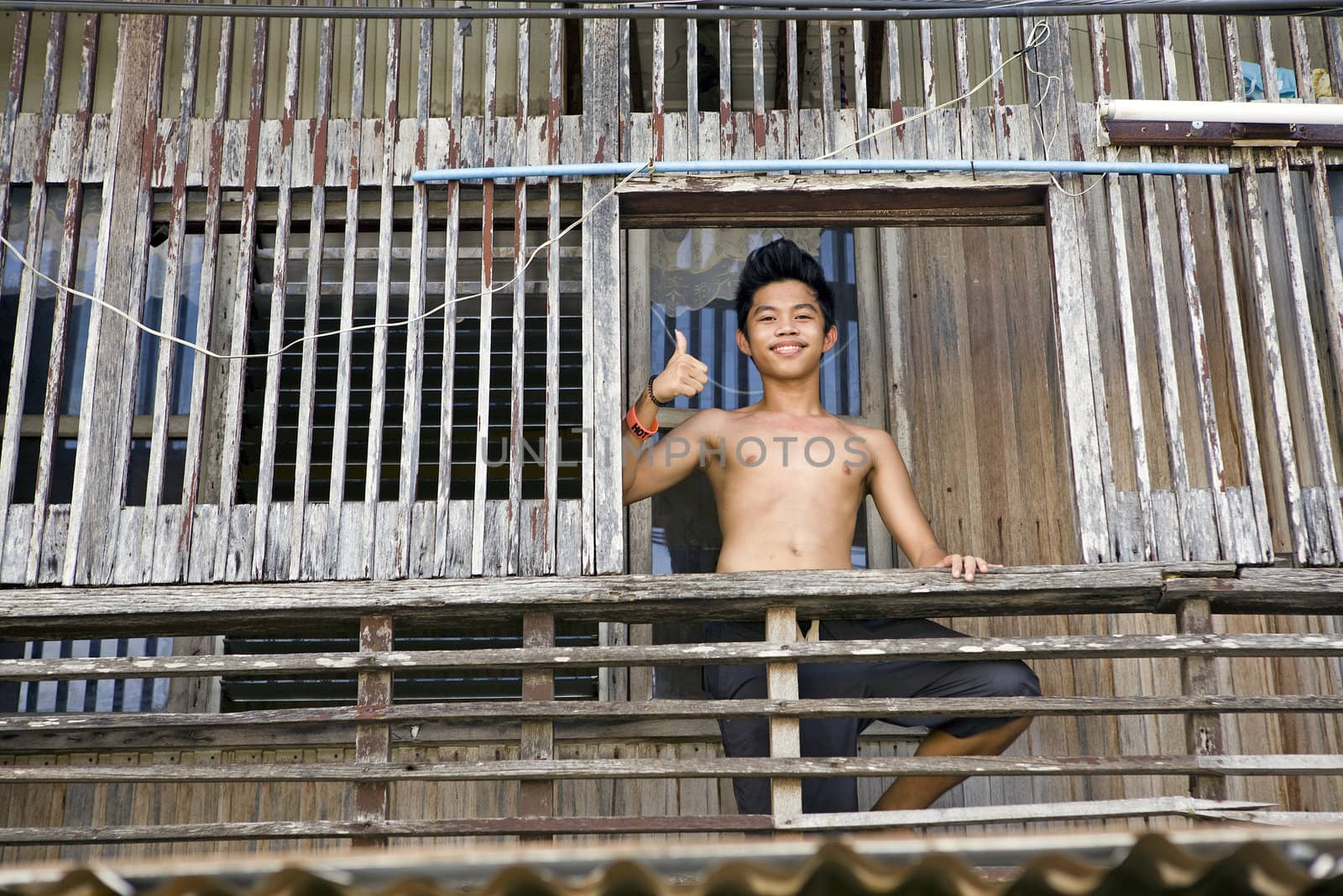 April 2012 - Bogo City, Panay, Philippine Islands - A smiling teenage Filipino boy giving thumbs up sign while standing on the porch of his traditional wooden style home in bogo City, Panay, Philippine Islands.