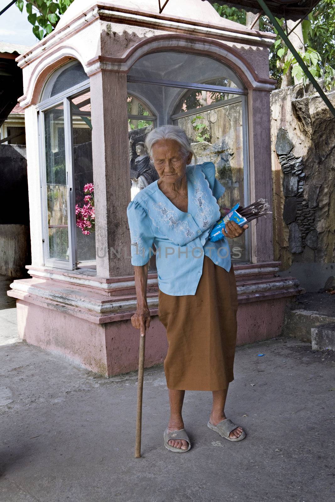 May 2012 - Bogo City, Cebu Island, Philippines - Elderly, blind Filipino woman walking with a cane selling votive candles near a Catholic christian shrine. Senior citizens are held in high respect in the Philippine culture no matter how old they are.