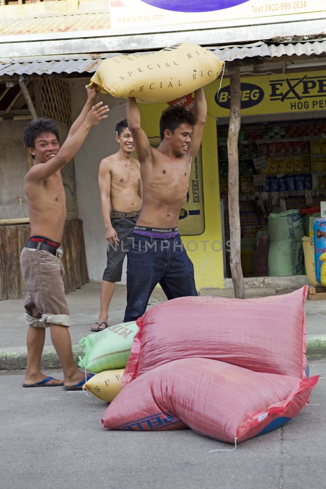 May 2010 - Bogo City, Cebu, Philippine Islands - Three teenage boys carrying 50 kilo sacks of white rice to a storage warehouse. Rice is the most important grain crop in the Philippine Islands.