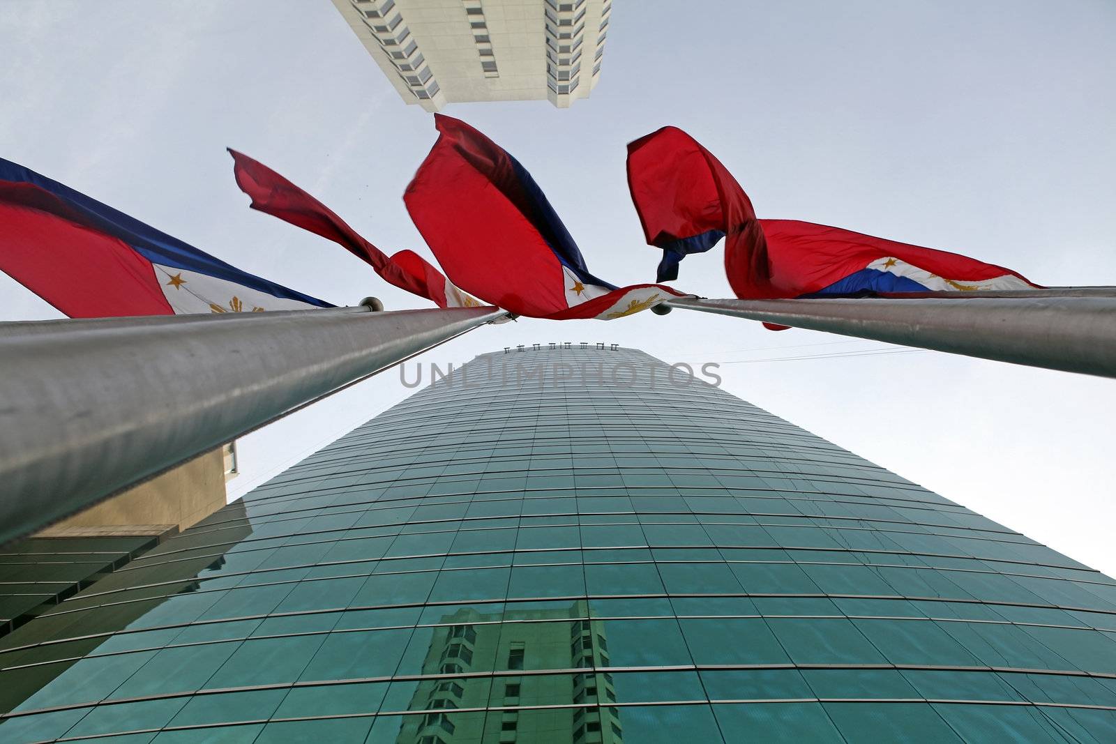 Manila City; Luzon; Philippine Islands - Four red, white and blue Philippine national flags waving in the wind in downtown Manila City on tall flagpoles. Modern skyscrapers border the flags. 