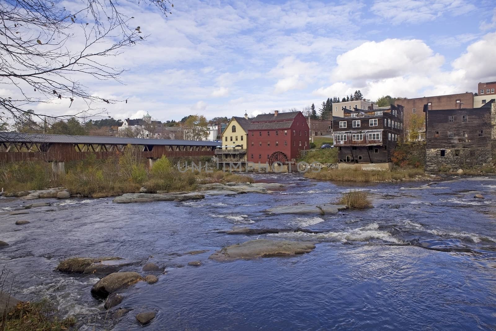 Ammonoosuc River flowing across rocks and under a covered bridge in Littleton, New Hampshire. An old grist mill and water wheel are near the bridge.