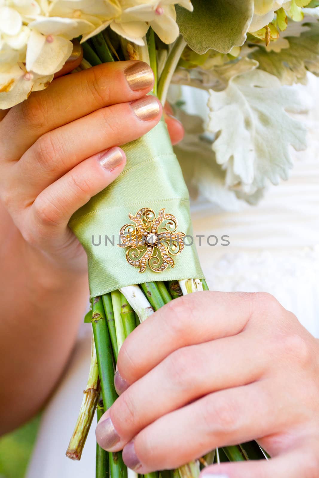 A bride holding her bouquet of flowers at her wedding ceremony with a meaningful brooch on the wrapping of the stems.