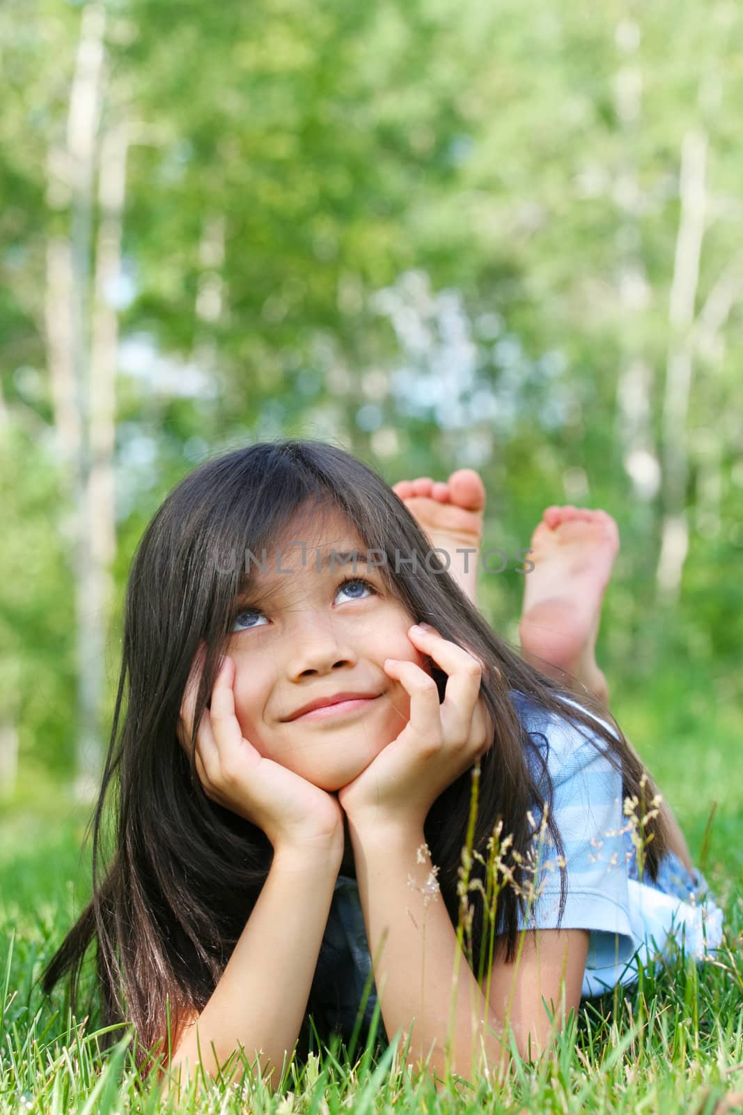 Little biracial girl lying on grass, looking up, thinking