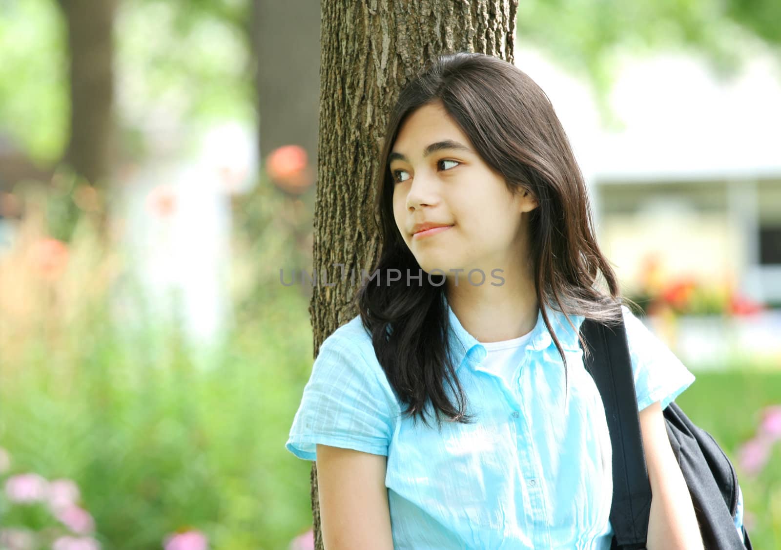 Young teen girl standing with backpack by tree, smiling. by jarenwicklund