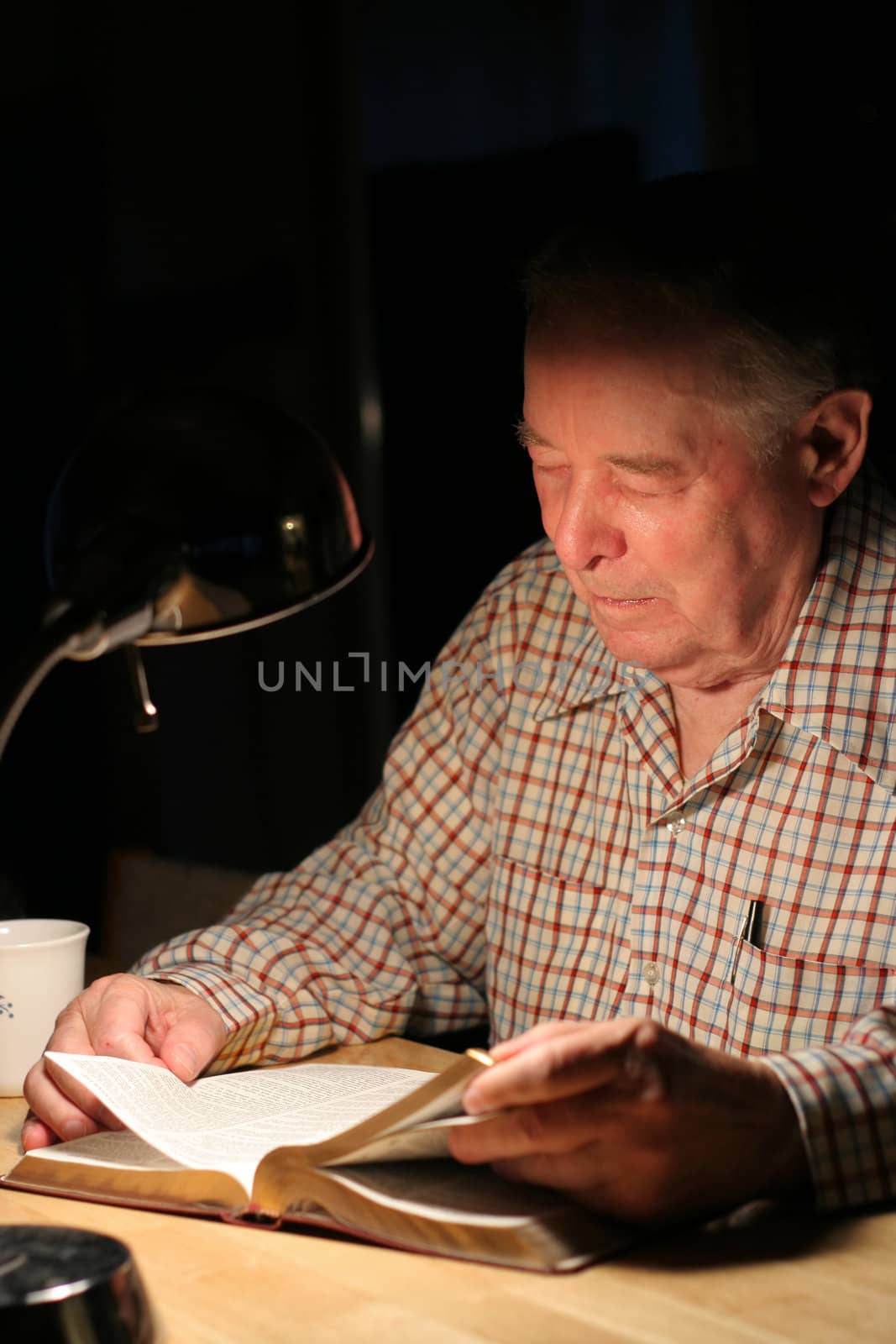 ELderly man reading Bible  with lamp at night by jarenwicklund