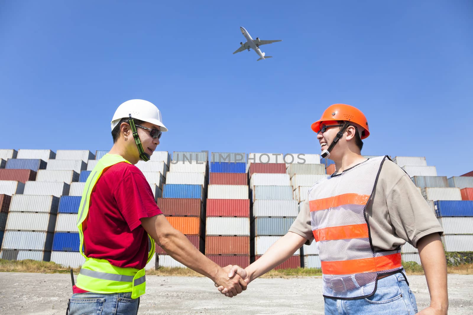 two happy workers handshaking before transportation containers by tomwang