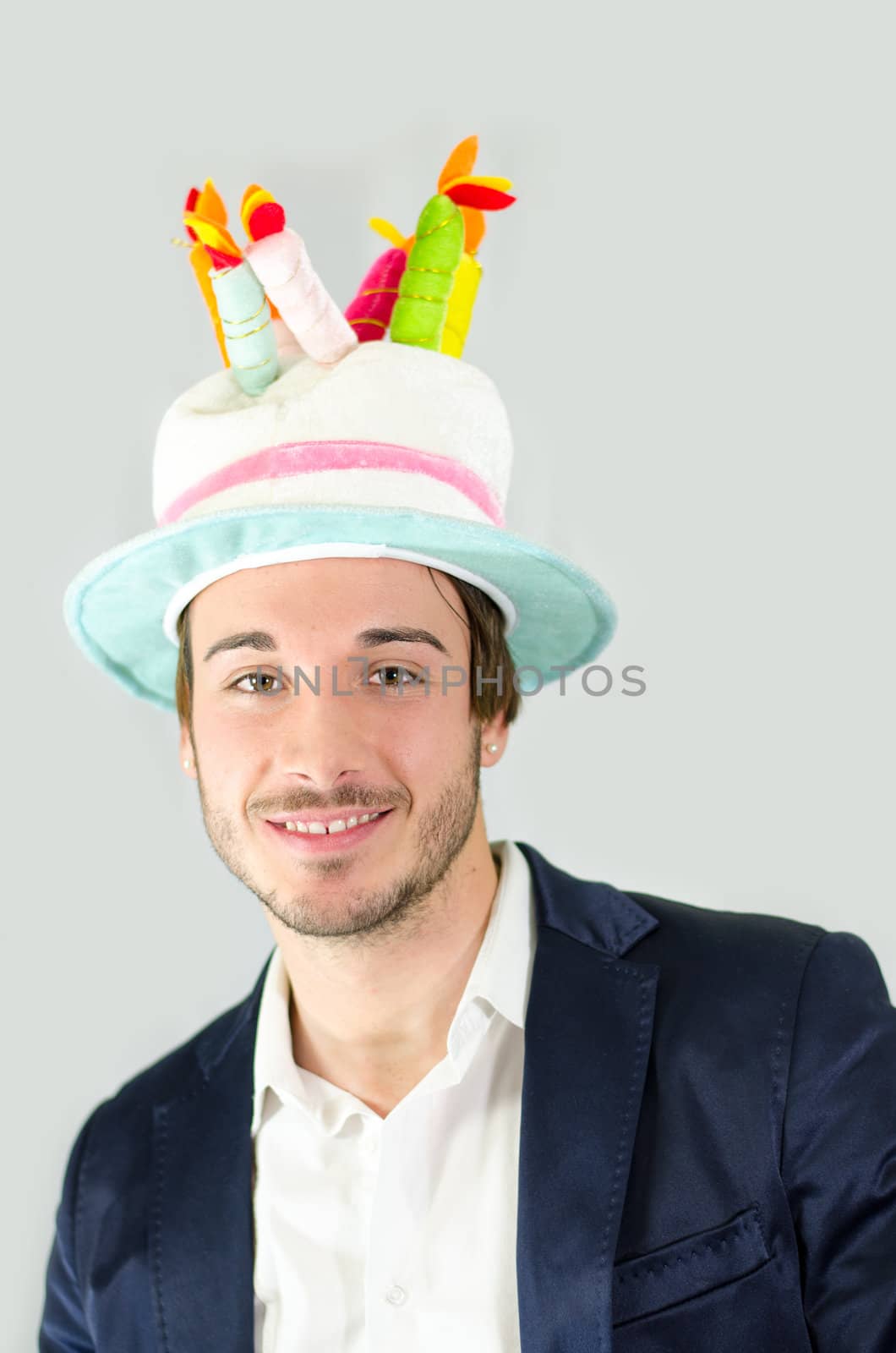 Cheerful, smiling, cute young man with funny birthday cake hat