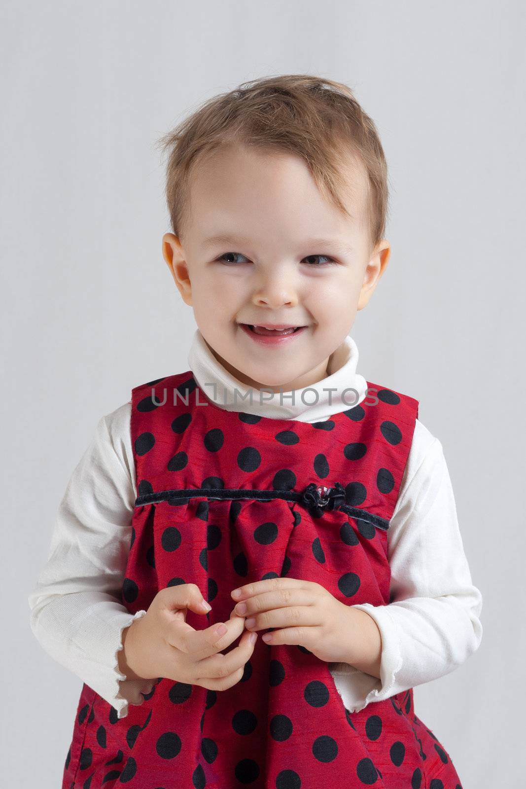 portrait of an smiling little blonde girl wearing a red dress with black spots