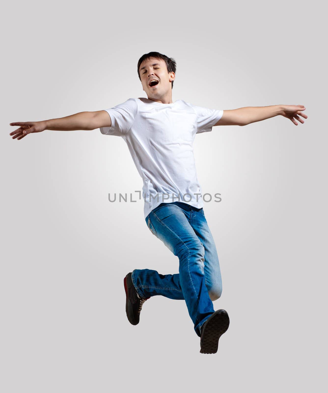 Modern slim hip-hop style man jumping dancing on a grey background