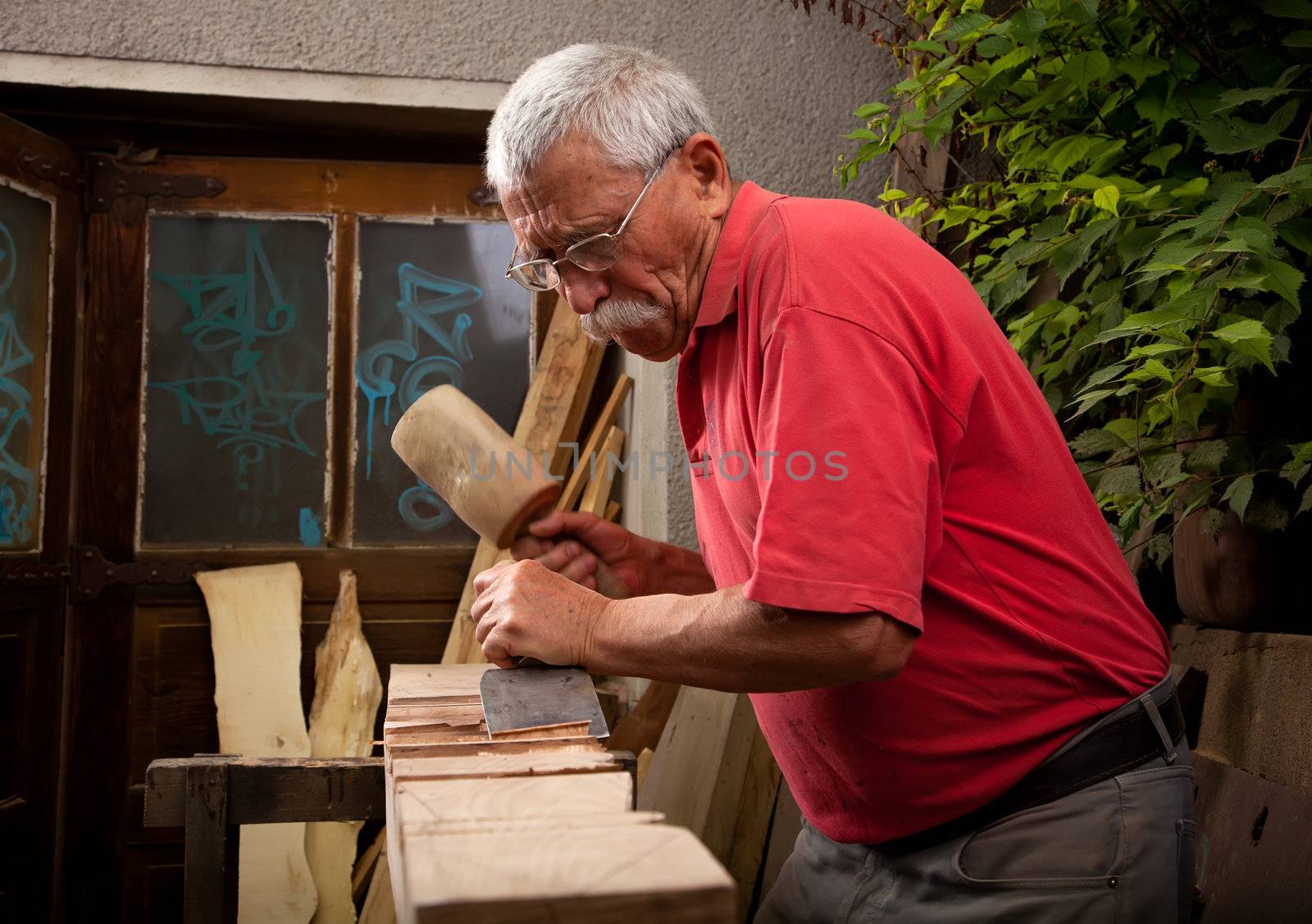 Old woodcarver working with mallet and chisel
