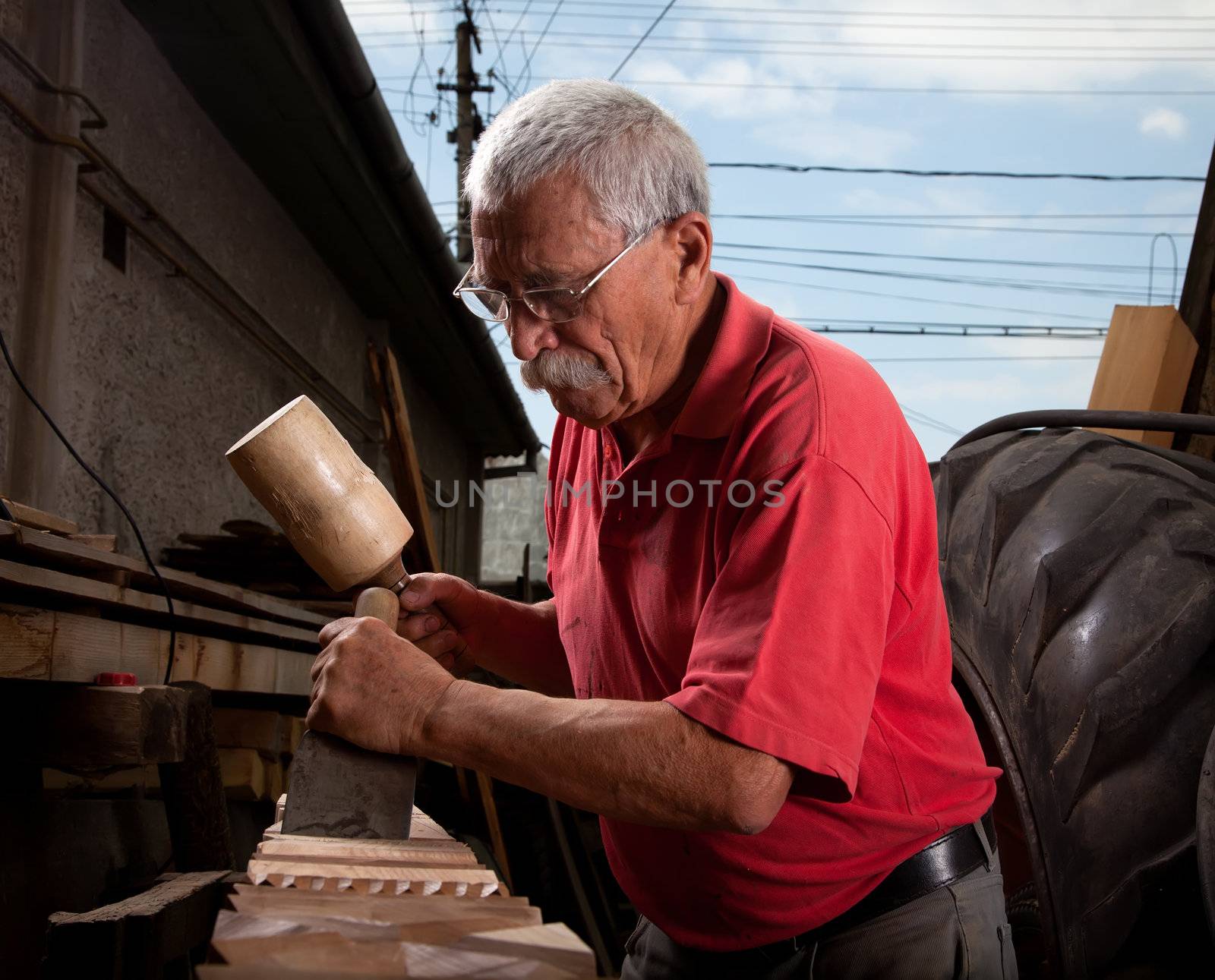 Old woodcarver working with mallet and chisel