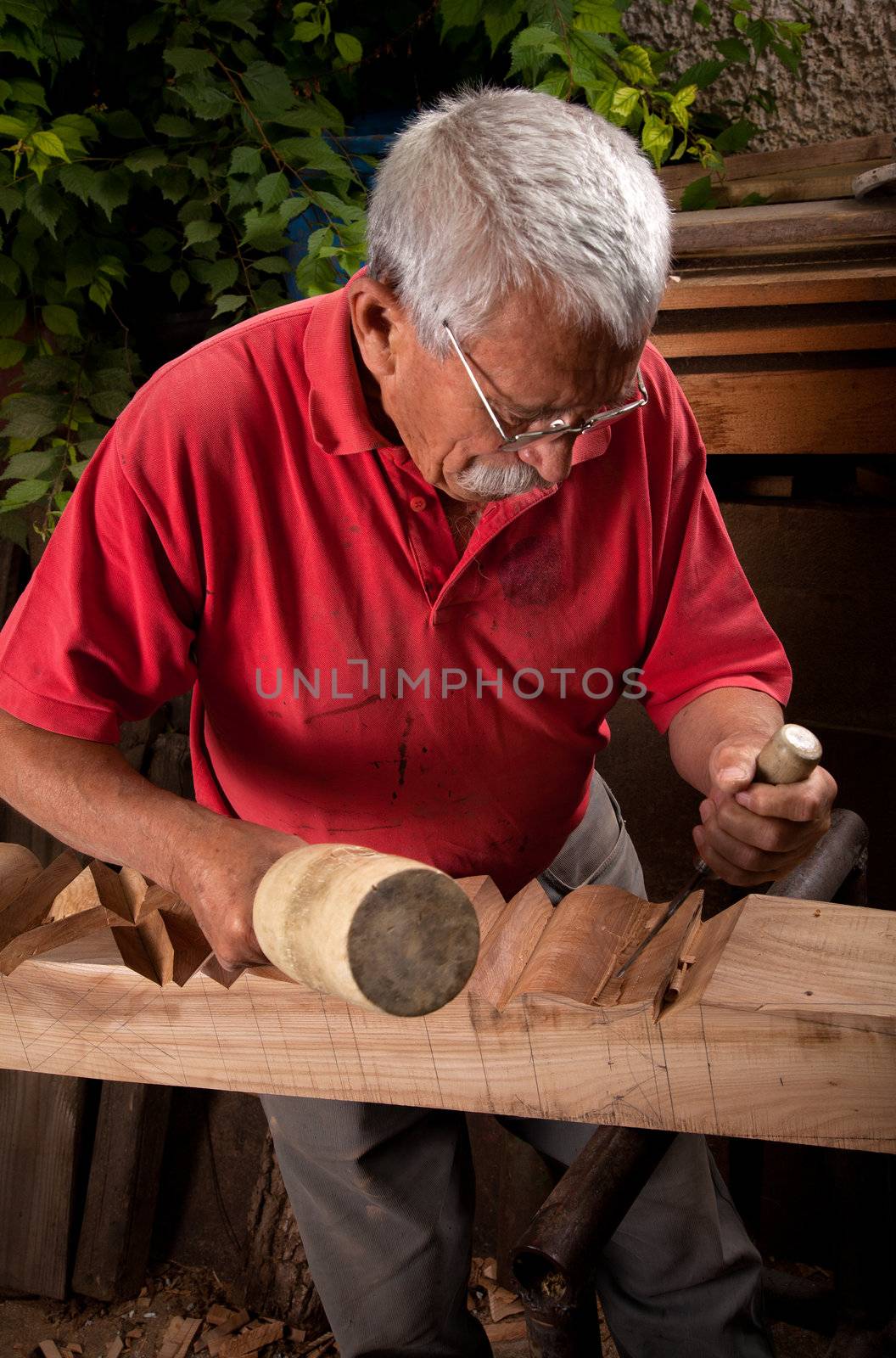 Old woodcarver working with mallet by ra2studio