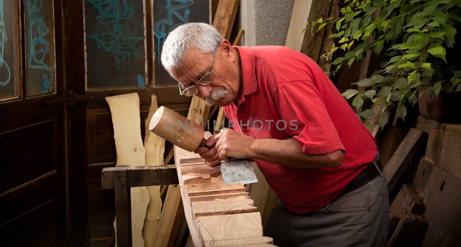 Old woodcarver working with mallet and chisel