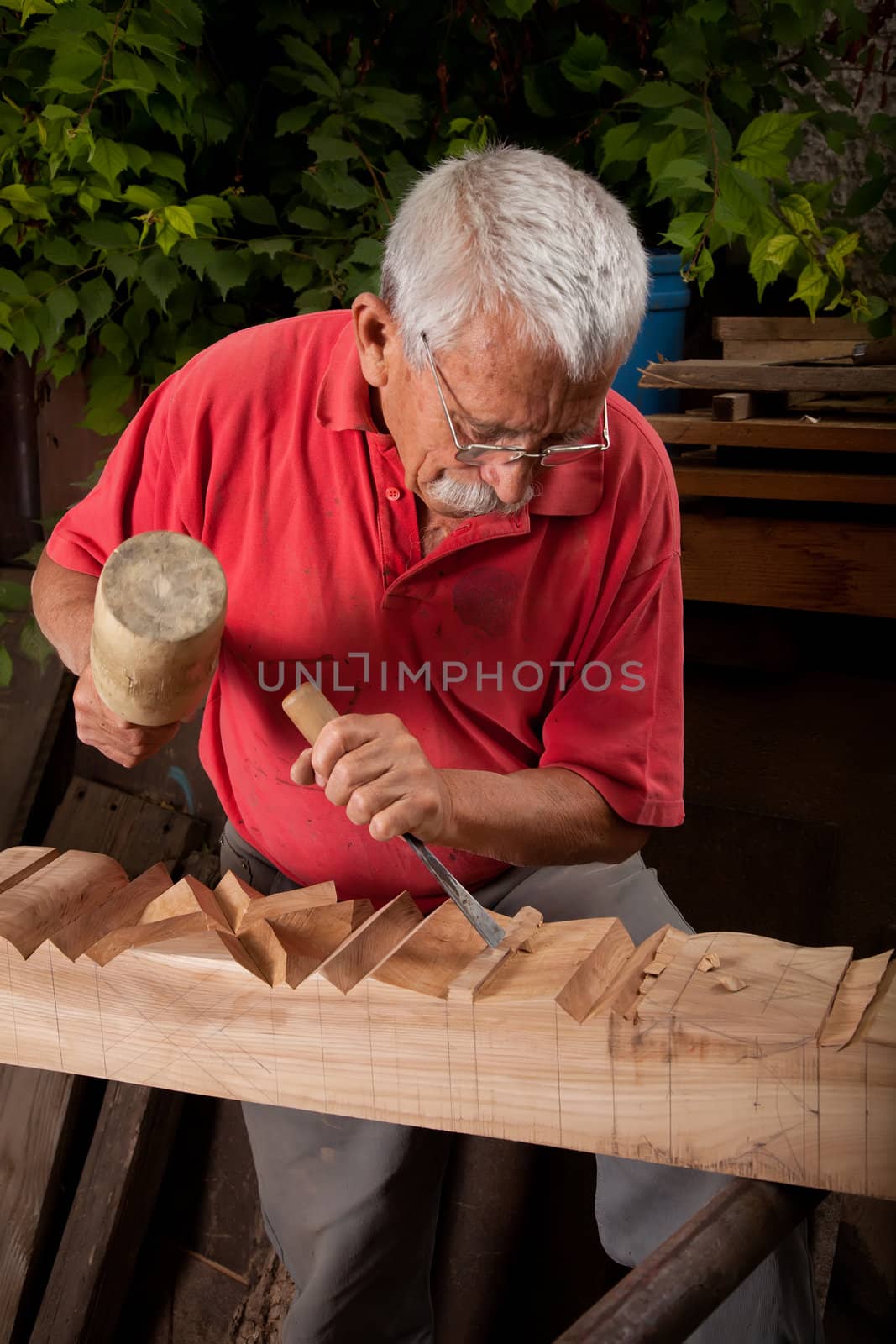 Old woodcarver working with mallet and chisel