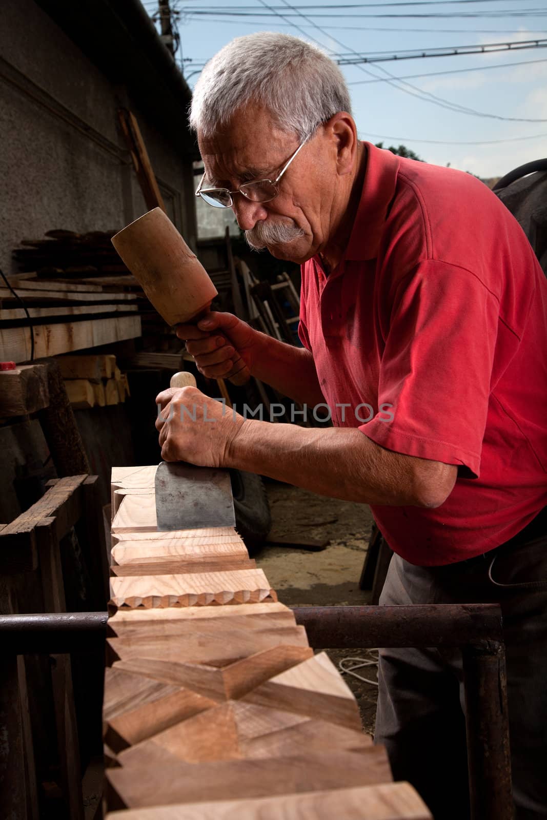 Old woodcarver working with mallet by ra2studio