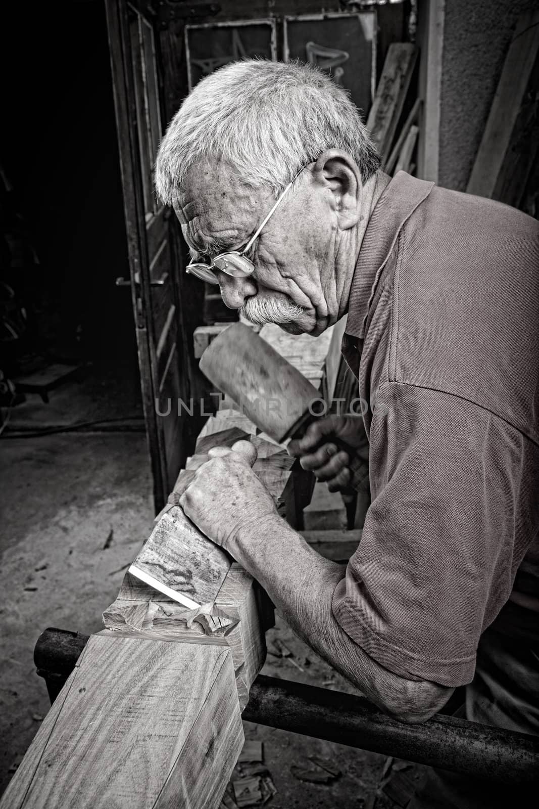 Old woodcarver working with mallet by ra2studio
