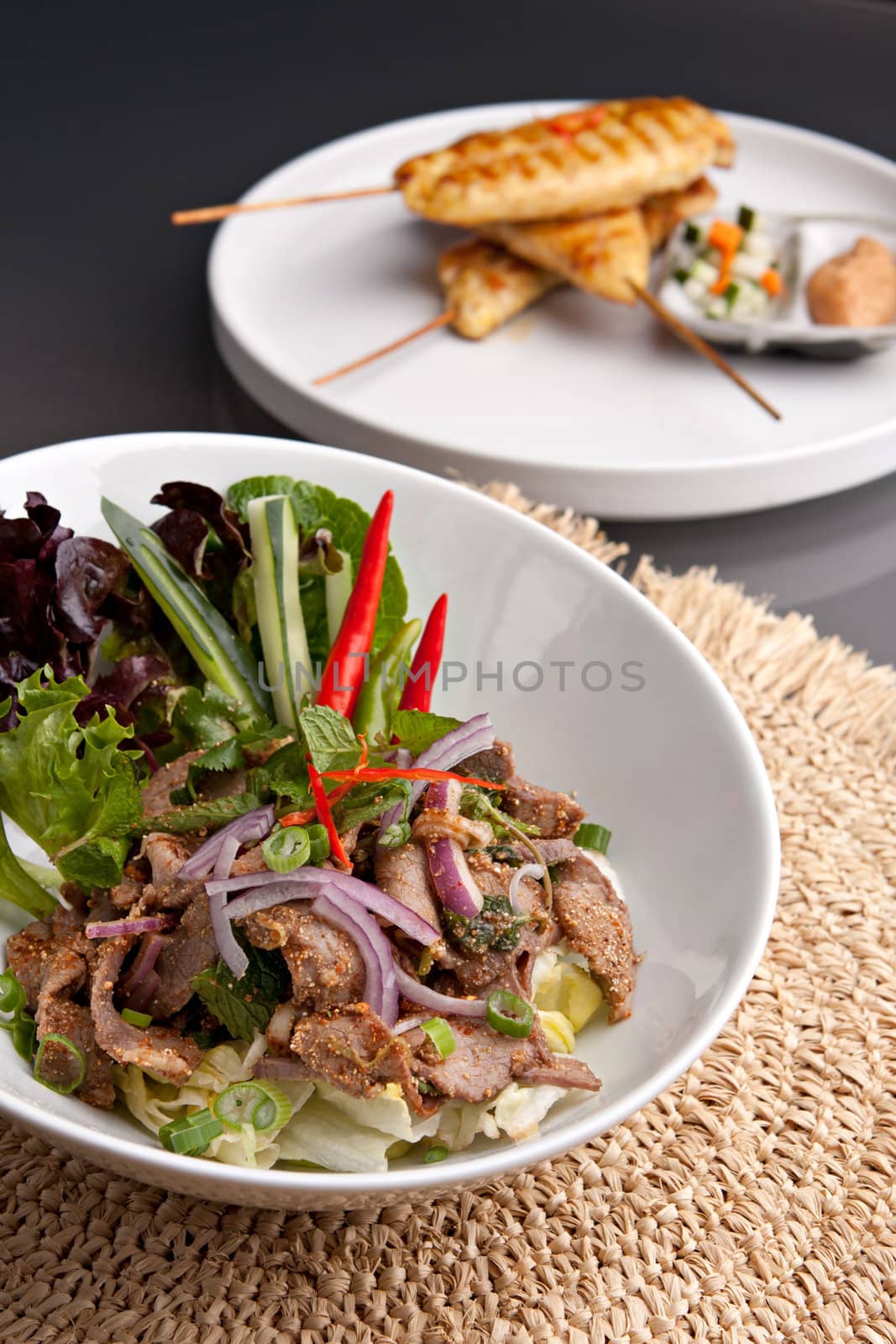 Asian style Thai salad with steak and chicken satay barbecued chicken on skewers appetizers in the background.