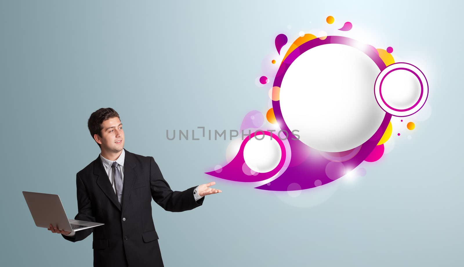 Attractive young man holding a laptop and presenting abstract speech bubble copy space 
