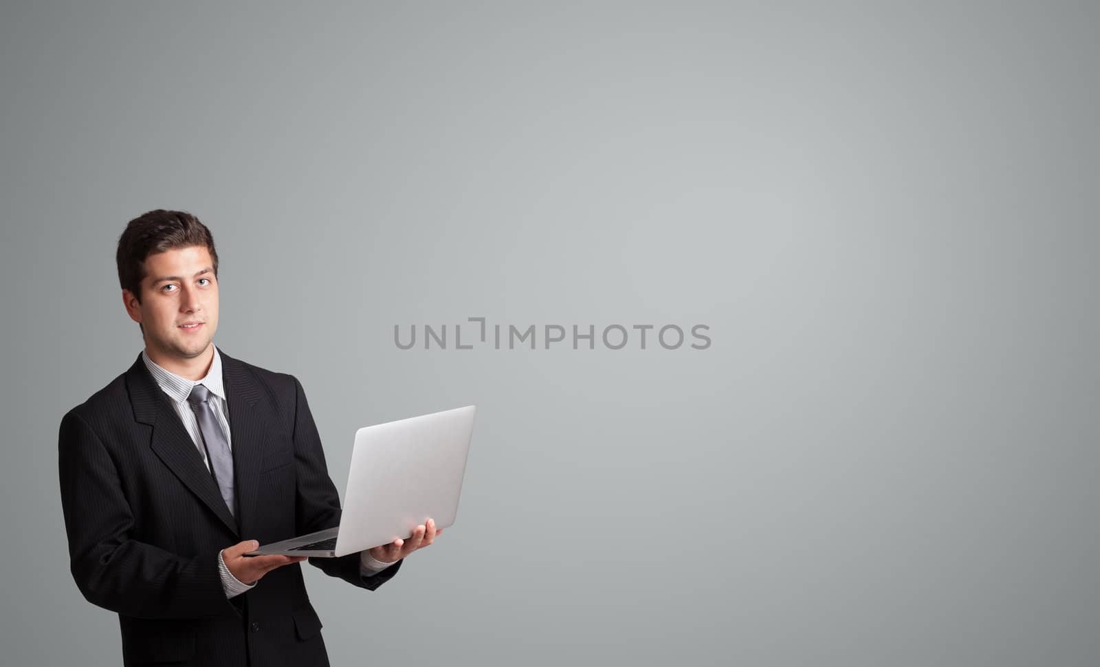 attractive young man holding a laptop and presenting copy space