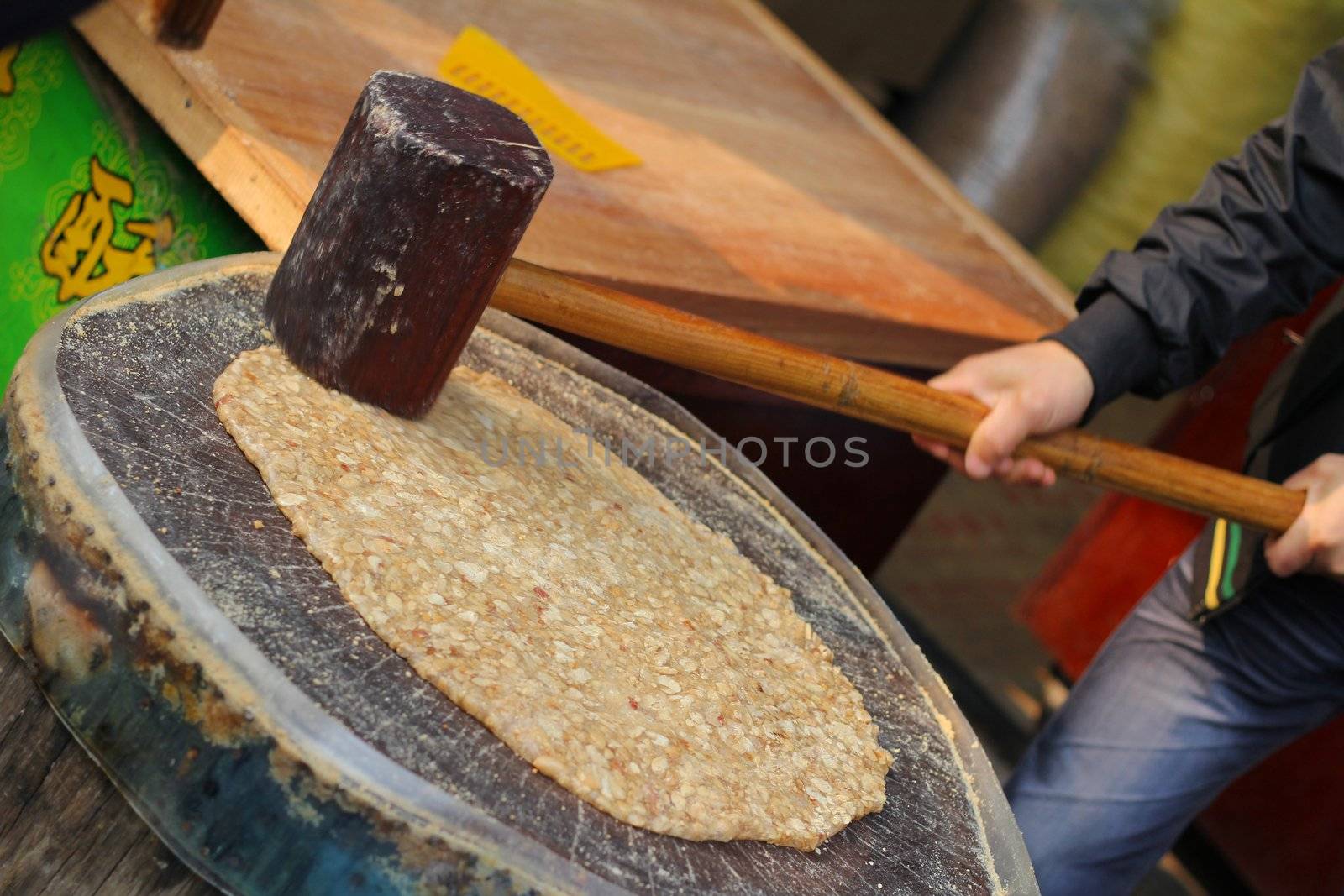 Traditional Chinese almond candy being prepared using wooden hammer on tree stump
