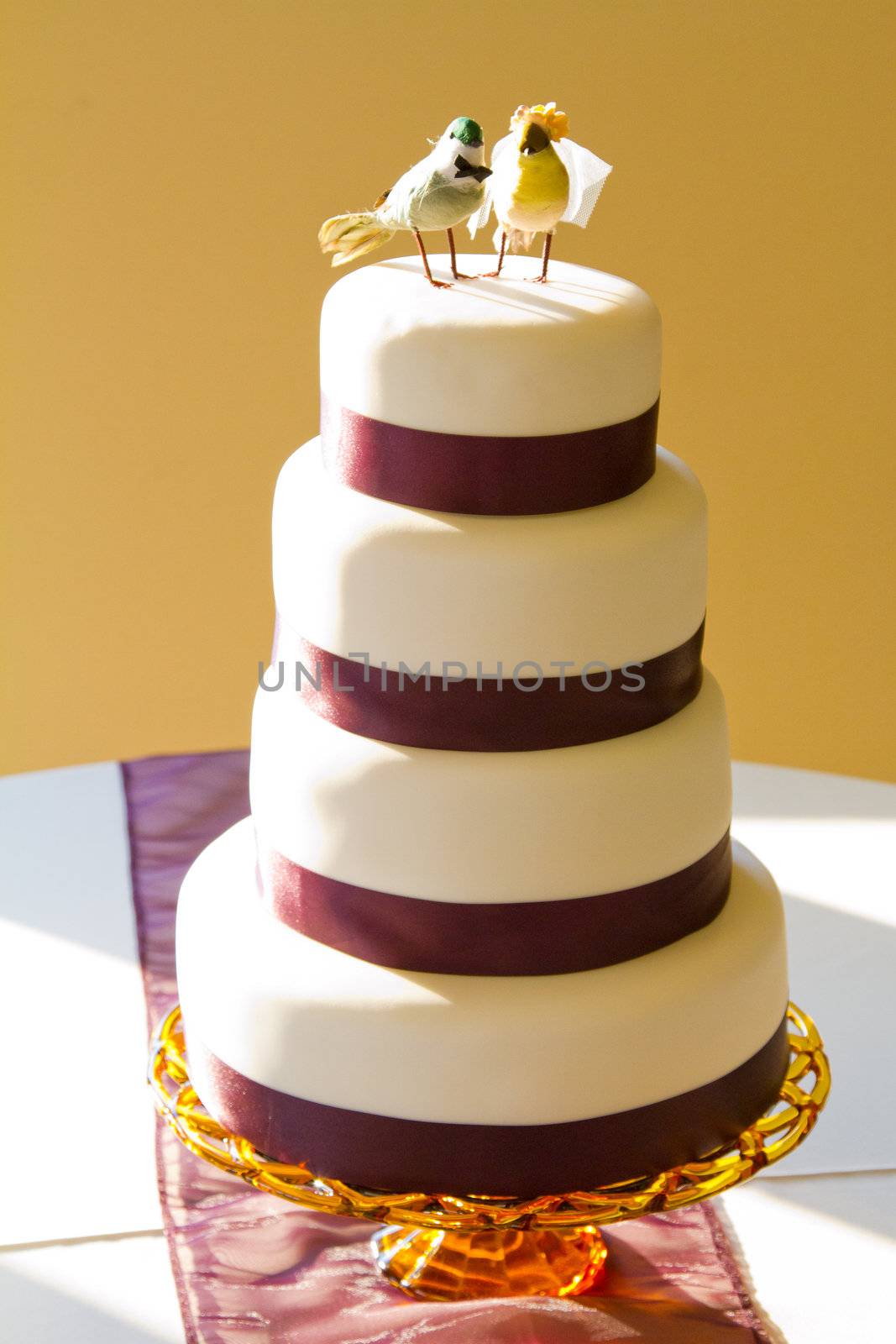 A traditional white wedding cake is topped with craft birds and wrapped in purple ribbon at the bride and groom's reception.